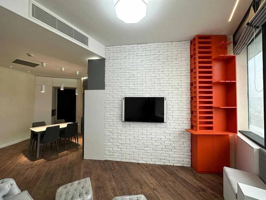 2-room apartment for sale on Ilia Chavchavadze Avenue, Vake, Tbilisi — living room with a white brick feature wall, wall-mounted TV and orange shelving unit